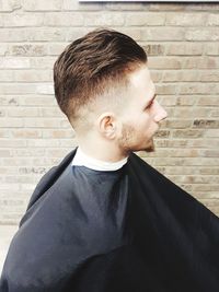 Young man sitting by brick wall at salon