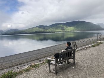 People sitting on bench by lake against sky