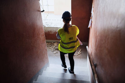 Rear view of female manual worker walking steps at construction site