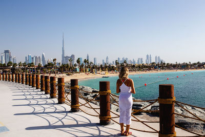 Rear view of woman standing by railing against sea during sunny day