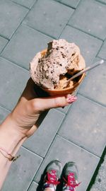 Low section of woman holding ice cream on footpath