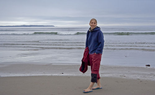Full length portrait of young woman standing at beach against sky