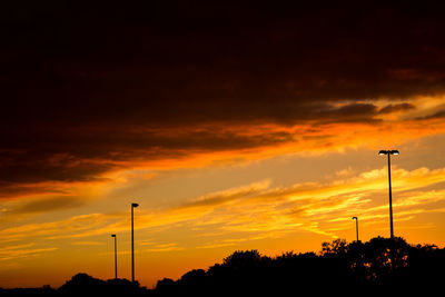 Low angle view of silhouette street lights against orange sky