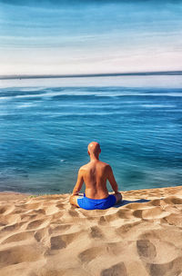 Rear view of shirtless man sitting on beach