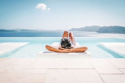 Woman relaxing on pool raft floating on swimming pool against sky