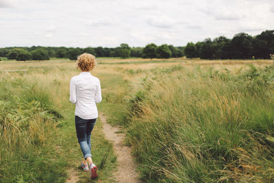 Rear view of young woman walking on grassy field