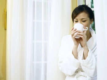 Woman drinking coffee while leaning on window