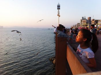 Girl standing by sea against sky during sunset