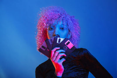 Portrait of young woman holding floppy disk against blue background