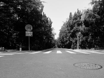 Road sign by trees against sky