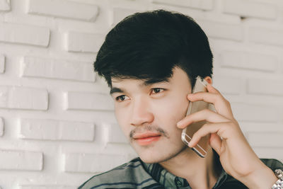 Portrait of young man using mobile phone against wall