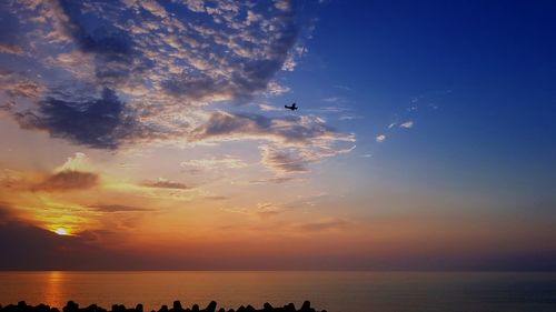 Silhouette airplane flying over sea against sky during sunset