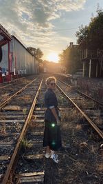 Man standing on railroad tracks against sky during sunset