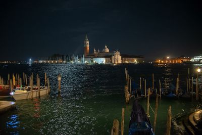 Boats moored in sea against illuminated buildings at night