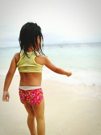 Rear view of girl standing at beach against sky