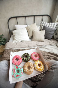 From above shot of anonymous barefoot female enjoying donut while sitting on comfortable bed 