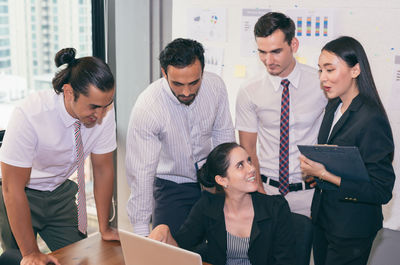 Businesswoman using laptop while explaining colleagues in meeting at board room