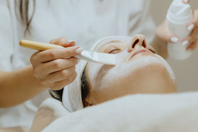 A girl cosmetologist applies a cream mask with a brush to a woman s face.