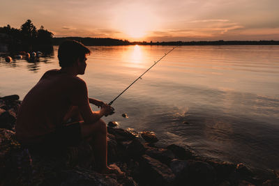 Adolescent boy fishing on shore of lake at sunset in ontario, canada.