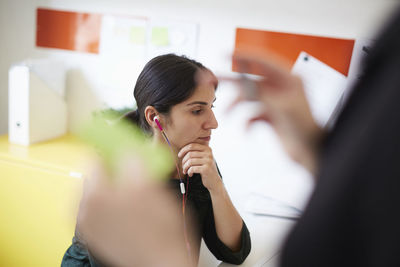 Mid adult businesswoman wearing earphones with colleague in foreground at office