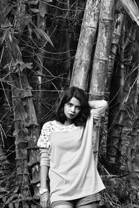 Portrait of woman standing against tree trunk in forest