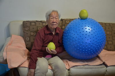 Senior man holding fruit by blue exercise ball on sofa at home