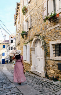 Young woman in pink dress walking in old town street, sightseeing, tourist, tourism, from behind.