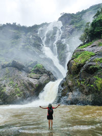 Full length of woman standing on rock against waterfall