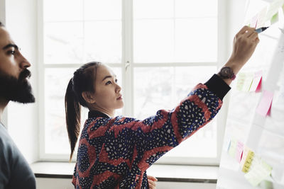 Female engineer writing on whiteboard and explaining colleague in office