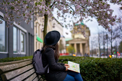 Side view of woman with map sitting on bench in park