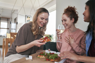 Smiling female friends eating food at home