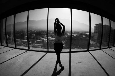 Full length rear view of woman standing by glass window in city