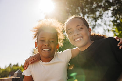 Portrait of smiling girls sitting with arms around at summer camp