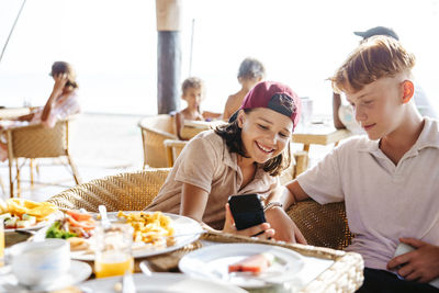 Happy girl sharing smart phone with brother at tourist resort during vacation