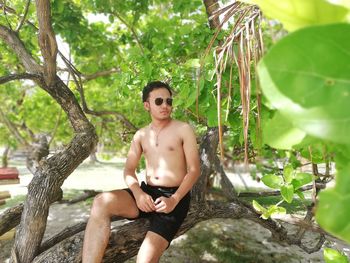 Young man sitting on tree trunk against plants