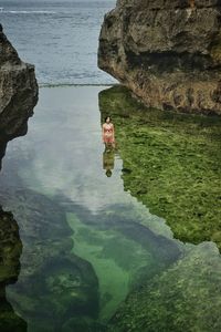 Reflection of woman on rock formation in sea