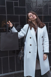 Portrait of woman holding bag standing against metal gate