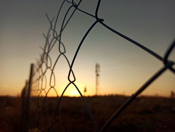 Close-up of barbed wire fence against sky during sunset