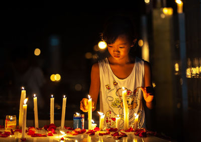 Girl igniting candles in darkroom at night