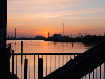 Silhouette railing by river against sky during sunset