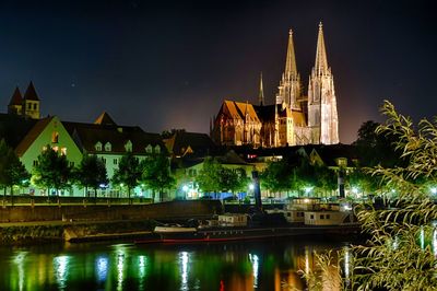 Illuminated buildings by river against sky at night