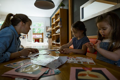 Mother assisting daughters in making crafts on table at home