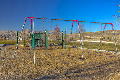 Empty swing in playground against clear blue sky