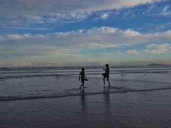 Friends walking at beach against sky