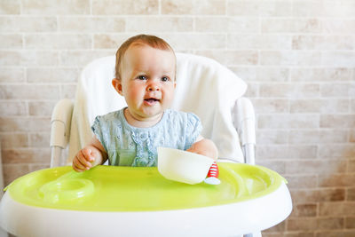 Cute baby girl sitting on high chair against wall