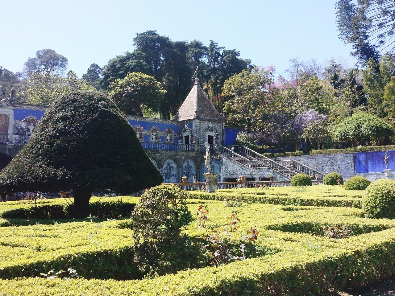 tree, architecture, built structure, building exterior, clear sky, statue, religion, famous place, art, art and craft, sculpture, place of worship, travel destinations, spirituality, park - man made space, growth, grass, history, human representation, formal garden