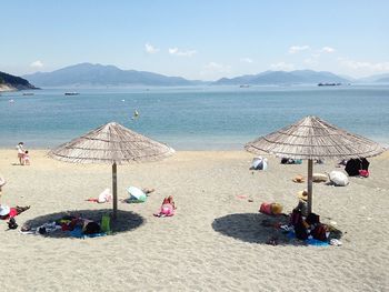 People relaxing by parasols at beach against sky