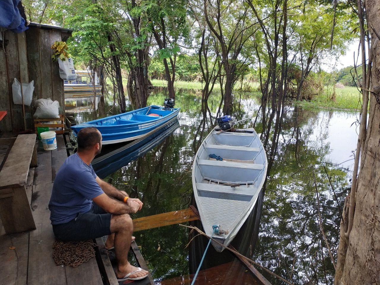 MAN SITTING ON BOAT AGAINST TREES