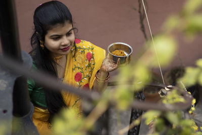 An indian woman in yellow saree is holding a bowl of turmeric paste during indian bengali marriage