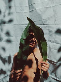 Portrait of man holding leaf against wall